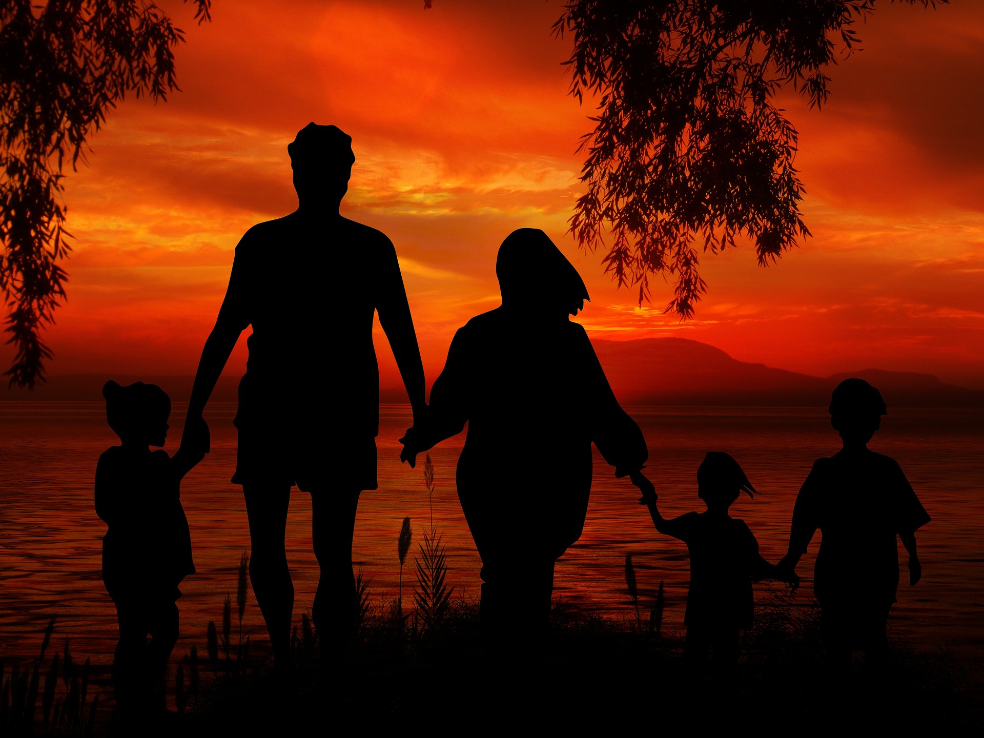 Pięciosobowa rodzina trzymająca się za ręce na tle czerwonego nieba od zachodzącego słońca