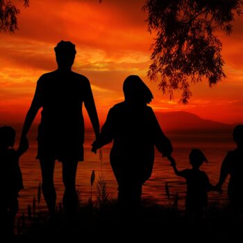 Pięciosobowa rodzina trzymająca się za ręce na tle czerwonego nieba od zachodzącego słońca